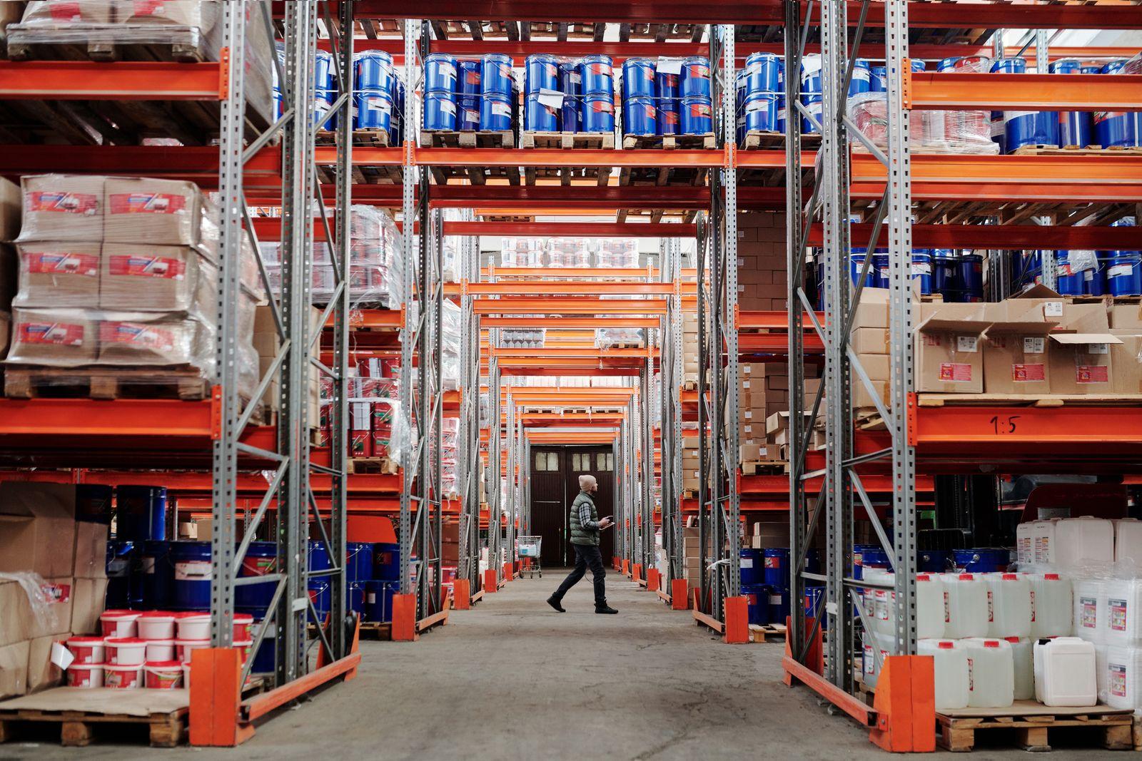 A worker walking down a warehouse aisle between shelves stacked with stock